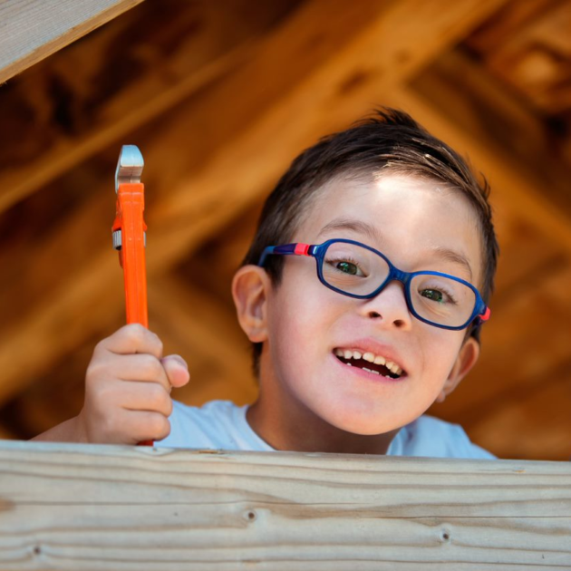 A young boy with glasses holding a paint brush.